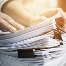 A person's hands on top of a stack of paper clipped white papers