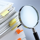 Magnifying glass pointed at a stack of marked papers